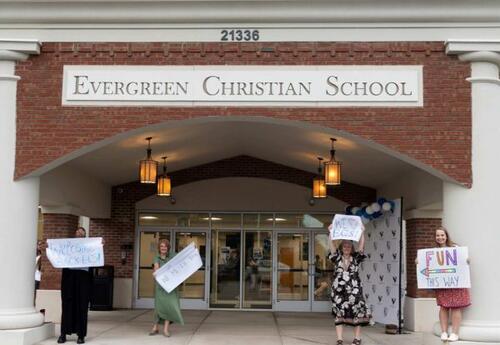 Teachers holding Welcome Back Signs in front of the school