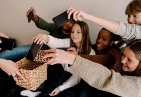 Teenagers putting cell phones in a basket