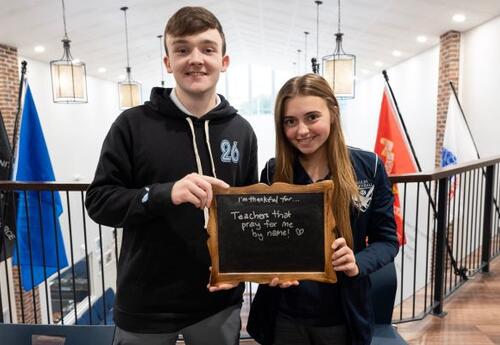 Photo of two students holding a sign that says they are thankful their teachers pray for them