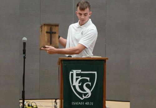 Student Holding a Box with a Cross on It and Reading the Bible