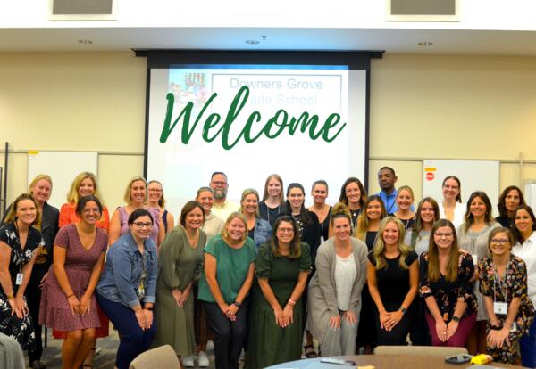 A group of 30 new teachers standing before a welcome sign