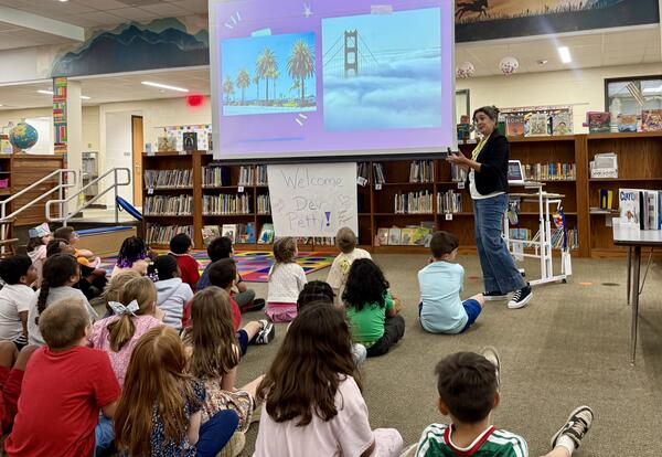Students sitting on floor watching adult speaking at front of room