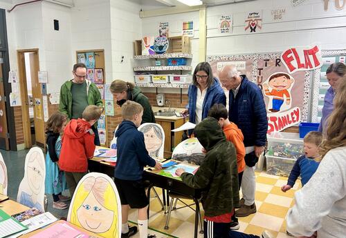 Families in classroom with students looking at student work on display on desks