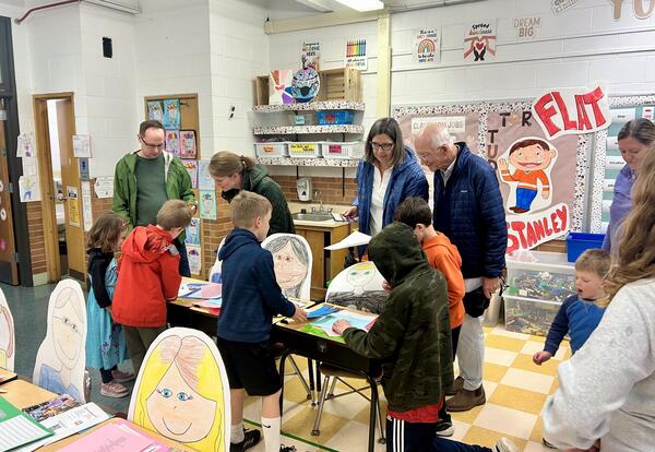 Families in classroom with students looking at student work on display on desks