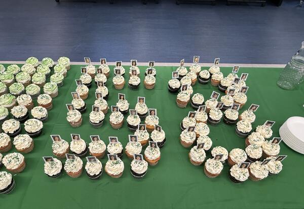 White frosted cupcakes with student photo picks in shape of "58" on a green tablecloth