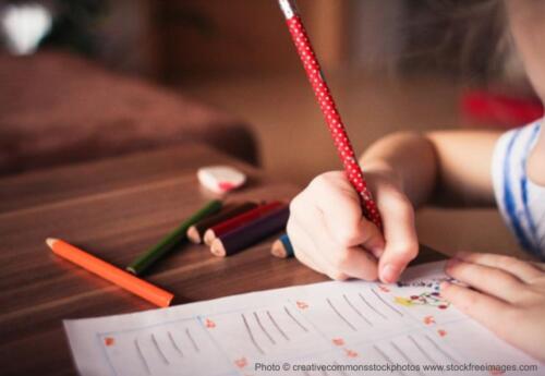 Student writing with colored pencils on worksheet at desk.