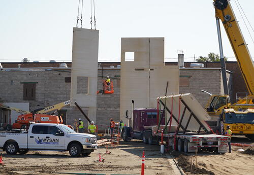 Picture of the construction site. Workers are putting up a pre-cast wall with a crane