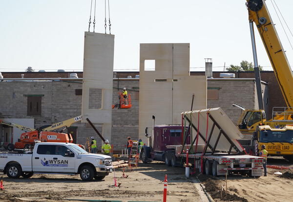 Picture of the construction site. Workers are putting up a pre-cast wall with a crane