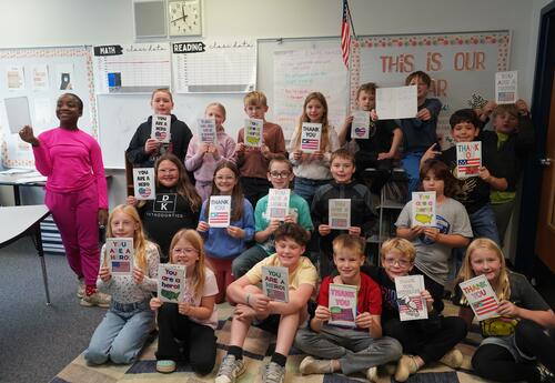 A third grade classroom holds up their cards for veterans