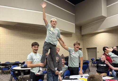 Two male students hold up another male at the conference