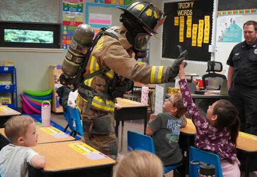 Firefighter in gear high fiving a student