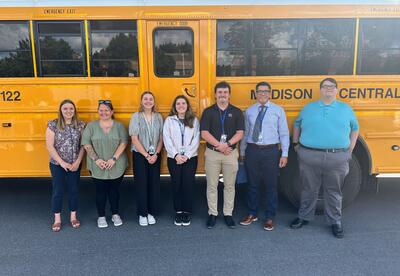 The newest members of the Madison Central School staff pose together for a photo in front of a school bus.