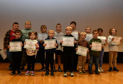 A group of students stand on stage while holding their award certificates.