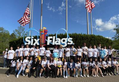 A group of students sitting and standing in front of the Six Flags sign.