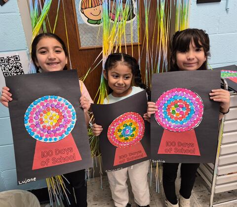 Three students posing with their artwork for the 100th Day of School