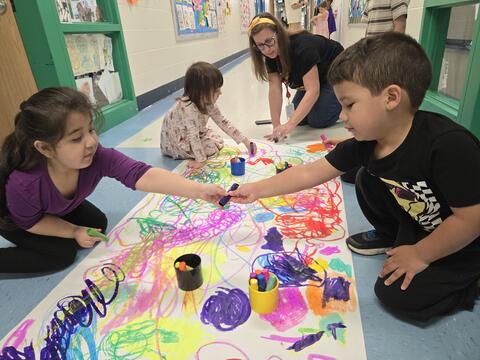 Students sharing a paint pen and painting on a large sheet of paper together