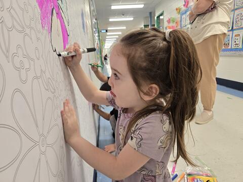 Girl using marker on a large paper with flowers on a wall
