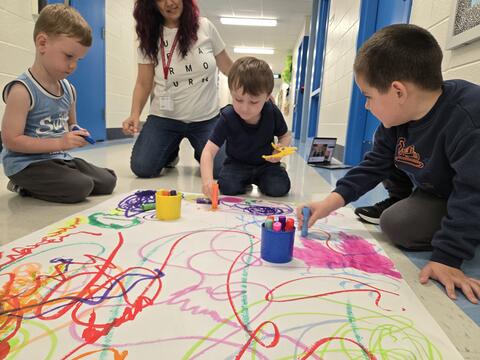 Group of students painting on a large sheet of paper in the hallway together