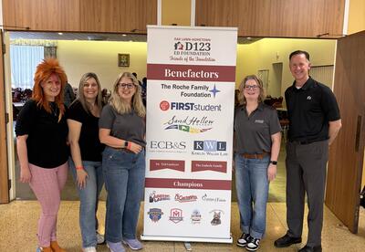 Members of the Educational Foundation stand smiling around the donation banner during the annual Tacos & Trivia event.