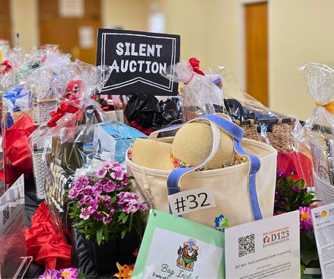 Table filled with various gift baskets and items wrapped in cellophane for a silent auction event indoors.
