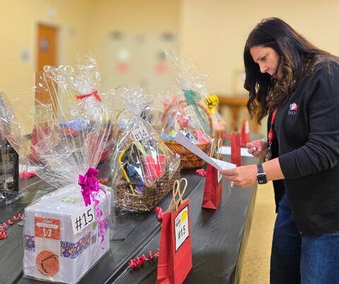 Woman reviewing a list while standing next to numbered gift baskets wrapped in clear plastic on a black table.