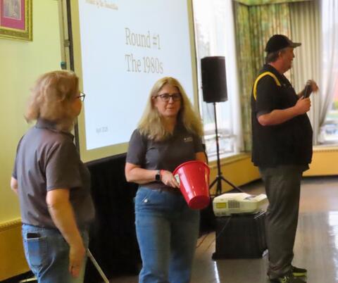 Three people in front of a screen for a trivia night, drawing raffle winners. 