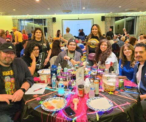 Group of people gathered around a table with snacks and drinks in a crowded room.