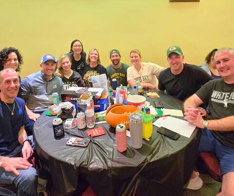 Group of people around a table with a black table cloth, covered in snacks and drinks
