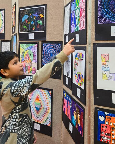 Child pointing at colorful abstract artwork displayed on a gallery wall with various vibrant drawings.