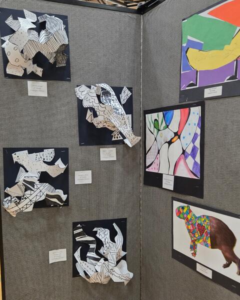 Display of 3-D and 2-D artwork on a gray wall.