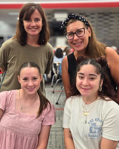 Four women smiling, two seated and two standing behind.