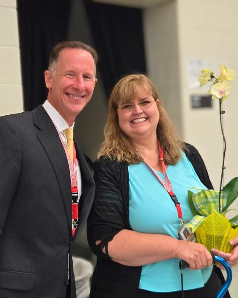 Two adults smiling with one holding a celebratory flower
