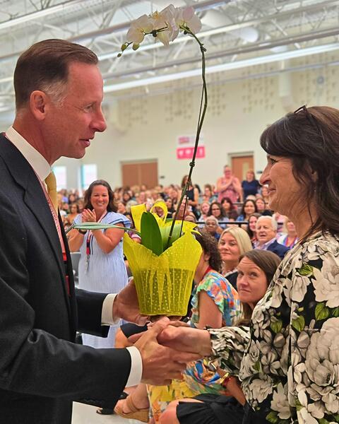 Women being recognized with a flower by a leader in front of a smiling crowd
