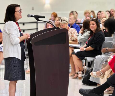 Women speaking at a podium in front of a large crowd.