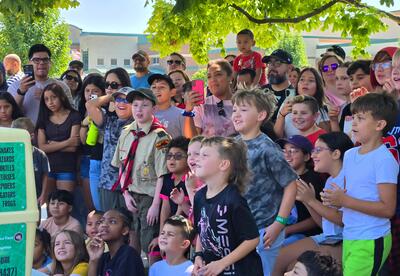 A diverse group of children and adult watching in amazement at an outdoor event.