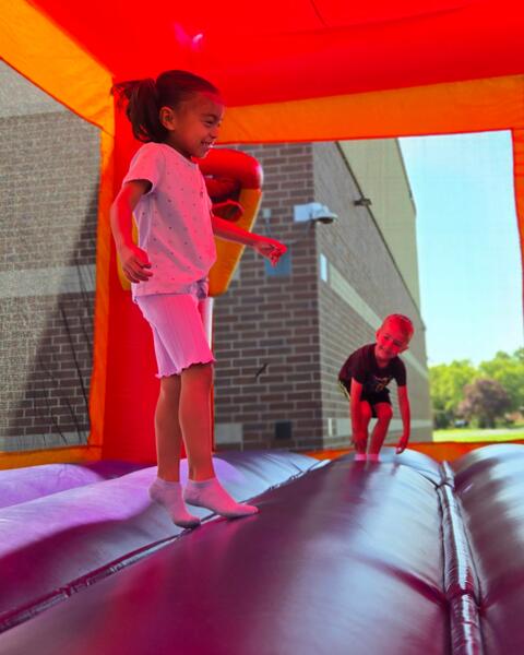 Young girl joyfully bouncing inside a brightly colored inflatable bounce house on a sunny day.