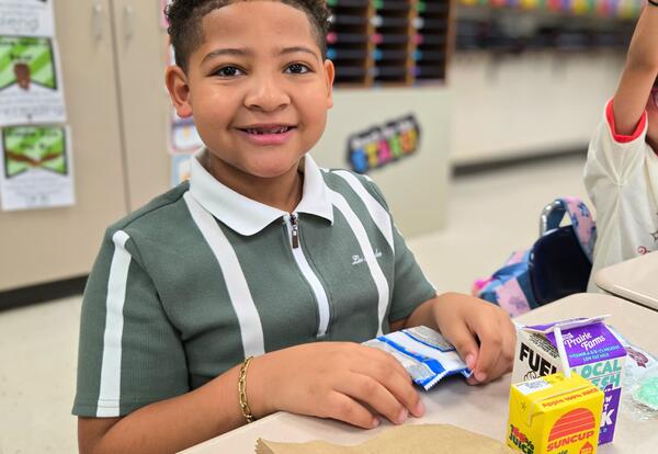 Child Smiling while enjoying breakfast foods and juice in a classroom setting.