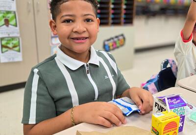 Child Smiling while enjoying breakfast foods and juice in a classroom setting.