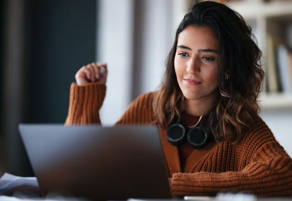 Here is a photo of a female student working on a laptop with headphones resting on her neck