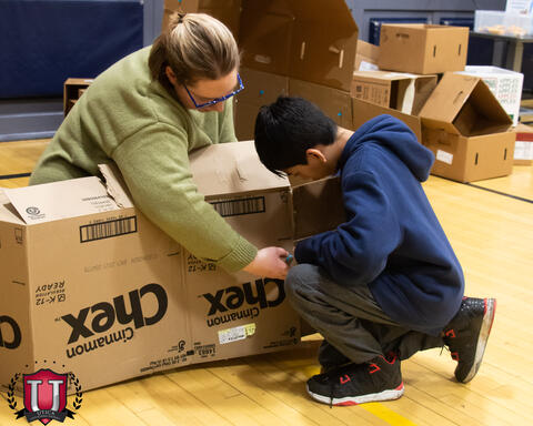 Staff helping student cut cardboard
