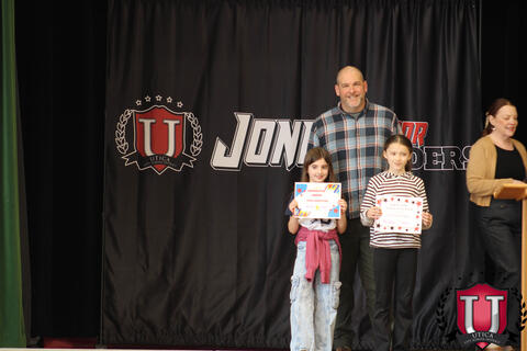 Two students posing with their awards as their teacher smiles with them
