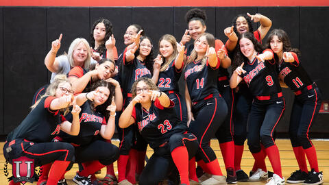 Softball girls pointing their hands out and fingers while posing