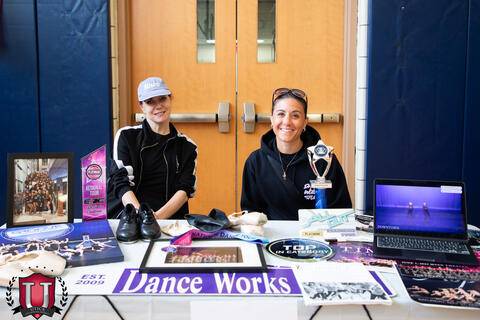 Two workers posing with their dance group pop up table