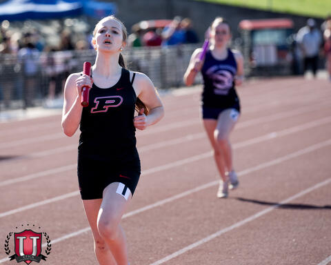 Athlete running with baton while another athlete trails behind her