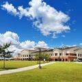 Exterior view of Fletcher Technical Community College’s main campus in Schriever, Louisiana, showing modern academic buildings, green lawns, walkways, and a clear blue sky with scattered clouds.