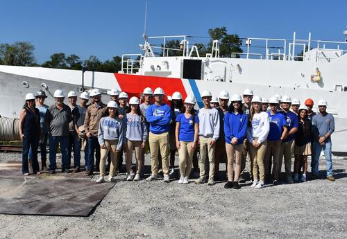 Photo of students at Bollinger with a ship in the background.