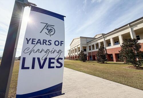 Campus banner celebrating 75 years of Fletcher Technical Community College with the text “75 Years of Changing Lives.” The banner is displayed on a light pole along a sidewalk in front of a Fletcher campus building on a sunny day.