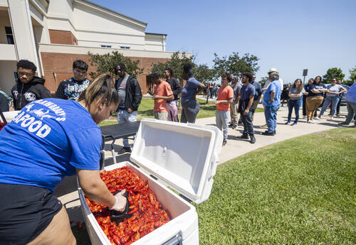A person serves crawfish from a cooler to a line of students gathered outside on Fletcher Technical Community College’s Schriever Campus during the 2025 Spring Fling event.