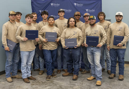 Group photo of Fletcher Technical Community College Line Worker graduates from the 2021 cohort, standing together in front of a Fletcher-branded backdrop and holding their certificates.