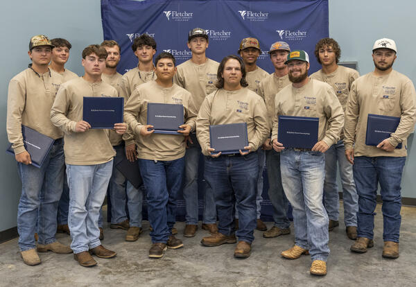 Group photo of Fletcher Technical Community College Line Worker graduates from the 2021 cohort, standing together in front of a Fletcher-branded backdrop and holding their certificates.